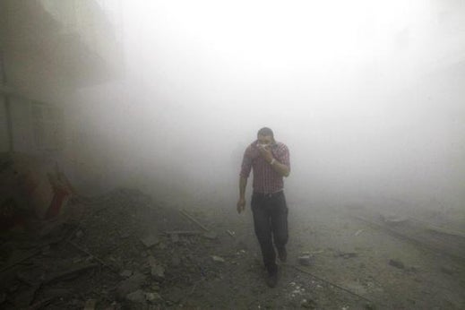 A man runs amongst rubble as smoke rises from buildings damaged by what activists said were missiles fired by a Syrian Air Force fighter jet loyal to President Bashar al-Assad in Raqqa province, eastern Syria, March 12, 2013.